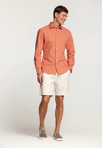 Punaste ja valgete triipudega kaelusega nööbitav särk, mille juurde on kombineeritud valged lühikesed püksid ja must-valgete ruuduliste mustade paeltega kingad.