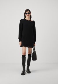 Abito nero in maglia con orlo in pizzo all'uncinetto, maniche lunghe larghe e scollatura sulla spalla. Abbinato a stivaletti neri al ginocchio e una borsa testurizzata.