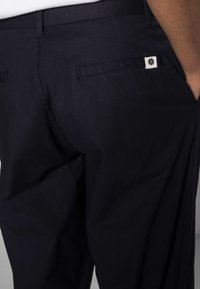 Marina byxor tillverkade av mjukt tyg med dubbla bakfickor och en liten logotyp ovanför den högra fickan. Skräddarsydd passform med sömmar på sidorna.