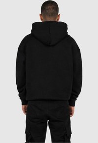 Zwarte hoodie met een grote capuchon, losse pasvorm en geribbelde manchetten. Gemaakt van zachte stof, met een schone achterkant zonder logo's of versieringen.