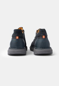 Pantofi din suede albastru închis cu o talpă gri, având accente portocalii pe spate și cusături, vârf rotund și un design cu profil redus.