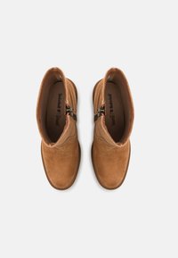 Bottines en daim marron avec une finition lisse, dotées d'une fermeture éclair sur le côté et d'un design à bout rond, sur fond blanc.