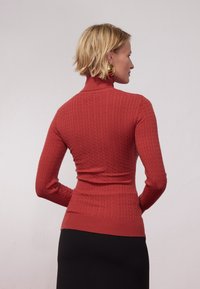 Red ribbed turtleneck sweater with fitted design, long sleeves, and textured knit. Worn with a solid black skirt, showing a sleek silhouette.