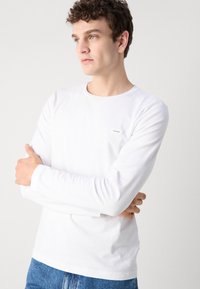 Hvit langermet T-skjorte med rund hals og en liten Calvin Klein-logo på brystet. Stylet med casual blå jeans.