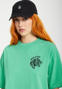 Zielona bawełniana koszulka z czarną grafiką lamparta i napisem "VOLCOM". W zestawie z czarną czapką z białym logo.