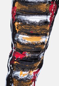 Jeans noirs déchirés avec de grandes déchirures et des accents peints en rouge, orange et blanc, créant une apparence texturée et superposée.