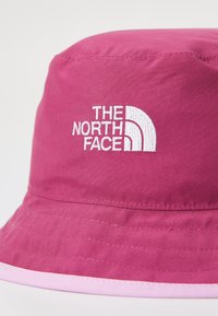 Rosa bucket hat gjort av mjukt tyg med en broderad vit logo av "The North Face" på framsidan och en kontrasterande rosa accent.