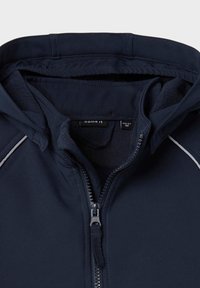 Námornícká bunda s měkkou fleecovou podšívkou, zapínání na zip a bílým kontrastním prošíváním na ramenou. Štítek viditelný uvnitř.