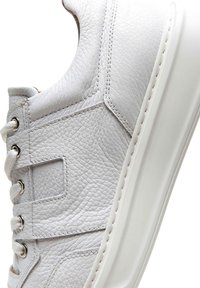 Sneaker bianca realizzata in pelle texturizzata, caratterizzata da un profilo basso, punta rotonda, lacci bianchi e occhielli metallici per un fissaggio sicuro.