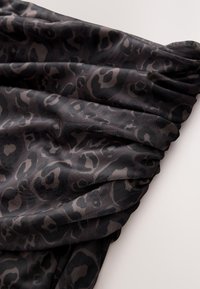 Tissu à motif léopard avec des nuances de noir et de marron ; texture douce avec un design froncé, créant des plis et une apparence dynamique.