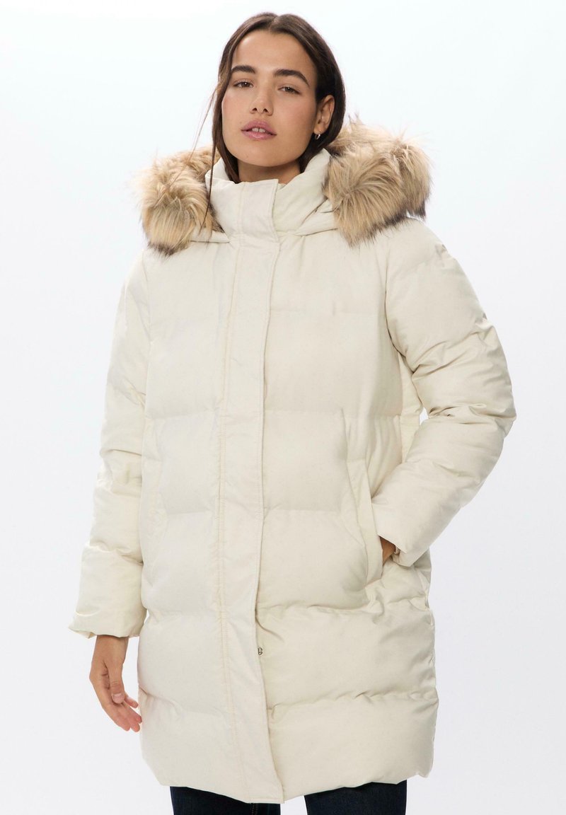 Bílá péřová bunda s odnímatelnou kapucí s kožešinovým lemováním, s prošívanou výplní a předními kapsami. Měkká textura a délka po kolena.