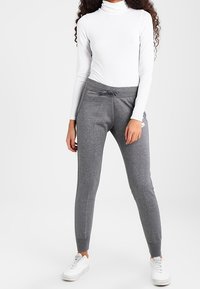 Gray jogger pants with a drawstring waist, paired with a white long-sleeve turtleneck. The pants have fitted cuffs and a smooth texture.