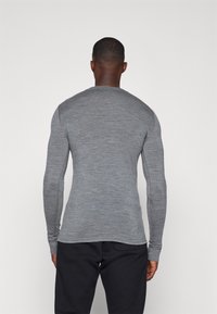 Camisa de manga longa cinza feita de um tecido suave e texturado, com um design ajustado e decote redondo. Apresenta costuras mínimas e sem padrões.