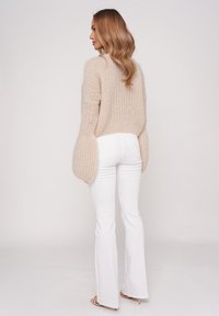 Beige fuzzy knit sweater with ribbed texture, wide bell sleeves; paired with fitted white jeans and beige heels. Simple, clean silhouette.