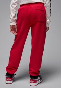 Punased fliisist püksid kummipaelaga vöökohas ja ühe tagataskuga. Kandjal on jalas mustade ja punaste toonidega tossud, millel on logo.