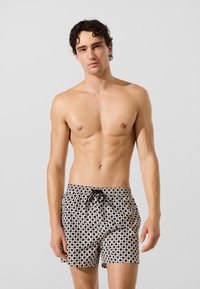 Mustvalged mustriga ujumispüksid, millel on elastne vöökoht ja pael. Disainis on ruudustikuna kirjamotiivid.