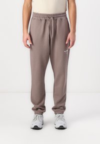 Grijze, elastische sweatpants met boorden; heeft een klein wit logo op de linker bovenbeen. Zacht stof, relaxte pasvorm, middelhoge taille.