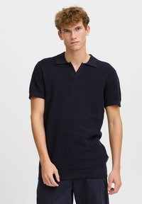 Navy polo shirt with a textured weave, short sleeves, and a V-neck collar. Features rolled sleeve cuffs and a straight hem.