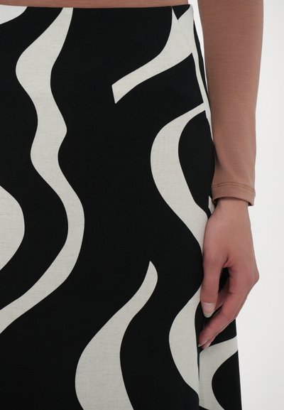 Jupe noire avec un motif ondulé blanc, en tissu texturé, avec une coupe légèrement évasée. Main positionnée près d'une couture latérale.