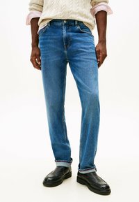 Blaue Denim-Jeans mit geradem Schnitt, ausgestattet mit einem klassischen Fünf-Taschen-Design und umgeschlagenen Säumen mit roten Nähakzenten.