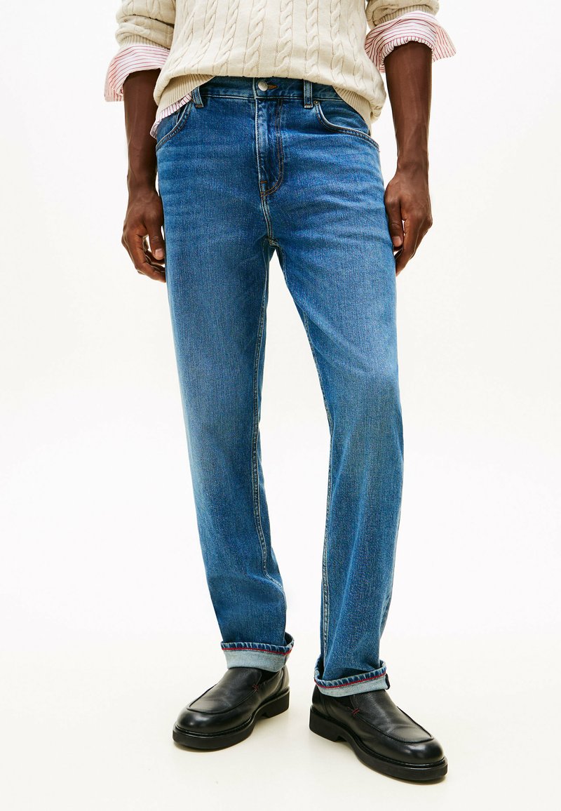 Blaue Denim-Jeans mit geradem Schnitt, ausgestattet mit einem klassischen Fünf-Taschen-Design und umgeschlagenen Säumen mit roten Nähakzenten.