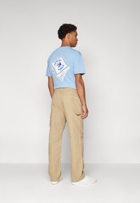 Blue cotton T-shirt with a graphic print on the back, paired with beige cargo pants. The shirt has short sleeves and a relaxed fit.