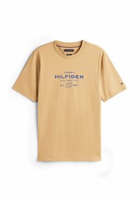 Beige bomulds t-shirt med korte ærmer og rund halsudskæring; har blå tekst "TOMMY HILFIGER NEW YORK CITY" og et lille logo på ærmet.