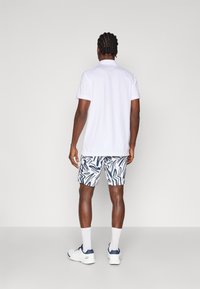 Camisa polo branca de manga curta com decote nas costas. Combinada com calções de banho estampados com designs abstratos em azul. Sapatos e meias atléticas brancas.