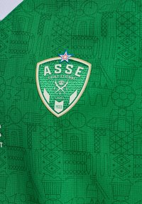 Camiseta deportiva verde con un patrón texturizado, logo de ASSE con una estrella y un elemento de diseño contrastante en acentos blancos y dorados.