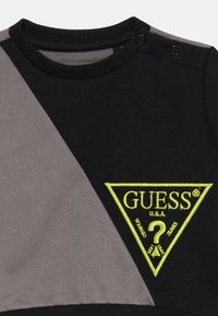 Crna i siva pamučna dukserica s trokutastim logotipom u neon zelenoj boji, s rebrastim okruglim izrezom i upečatljivim zatvaračima.