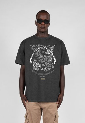 Dunkelgraues T-Shirt mit einem weißen floralem und tierischem Grafikdruck sowie einem kleinen Logo-Tag am Saum. Kurze Ärmel, lockere Passform.