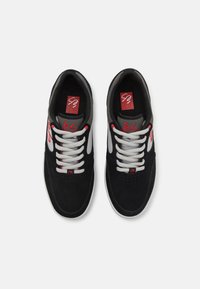 Baskets en daim noir avec des accents gris, lacets blancs et un logo rouge sur la languette. Bout arrondi et col rembourré pour le confort.