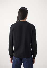 Sort, langærmet sweater med rund halsudskæring, ribbede manchetter og kant. Båret over blå denimjeans, der viser et simpelt, minimalistisk design.