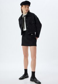 Ensemble en tweed noir comprenant une veste et une jupe avec un design court, des boutons en argent, et un motif à carreaux. Associé à une blouse blanche à volants et des mocassins noirs.