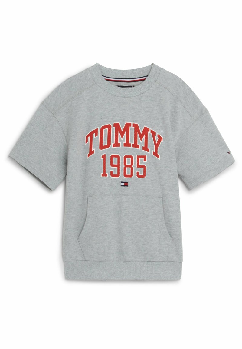 Felpa grigia oversize con maniche corte, caratterizzata dalla scritta "TOMMY 1985" in grassetto rosso. Include una tasca frontale e colletto a costine.