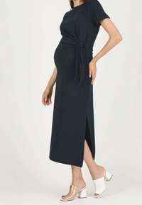 Gravidklänning i marinblått, knälång med sidoflik, knytdetalj i midjan, tillverkad av mjukt tyg. Bärs med sandaler med genomskinlig klack.