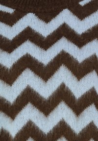 Braun-weißer Zickzack-Muster-Strickstoff, der eine weiche Textur mit kontrastierenden Farben und einem fluffigen Erscheinungsbild aufweist.