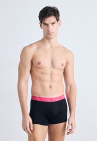 Boxer-briefs noirs avec une ceinture rose portant la marque "TOMMY HILFIGER". Le tissu semble doux, avec un design ajusté et élégant.