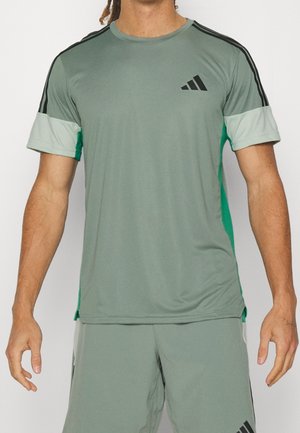 Mann trägt hellgrüne Adidas-Sportbekleidung mit schwarzen Streifen an den Ärmeln und Adidas-Logo auf Brust und Shorts.