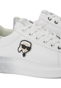 Valge nahkstklassik featuring hõbedase sädelevate tallade, musta kummist logo ja ümmargused silmad valgete paeltega. Sees pehme kangas vooder.