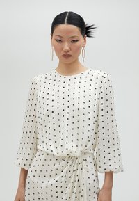 Vestido blanco de manga larga con lunares negros y textura a rayas verticales, con cintura fruncida y silueta fluida.