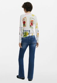 Long-sleeve white shirt featuring colorful floral and stamp prints, paired with dark blue flared jeans. Cotton and denim materials visible.