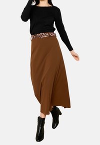 Bruine wikkelrok met een vloeiend ontwerp, voorzien van een riem met luipaardprint, gecombineerd met zwarte enkellaarsjes en een zwarte top met lange mouwen.