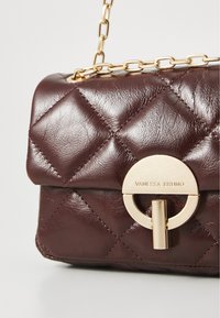 Sac à main en cuir matelassé bordeaux avec une chaîne dorée, doté d'un fermoir circulaire doré et du nom de la marque gravé.