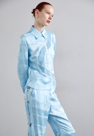 Cămașă din satin de culoare albastru deschis, cu guler, cu nasturi în față și un model curbat. Asortată cu pantaloni potrivitori, decorati cu ornamente colorate pe părți.