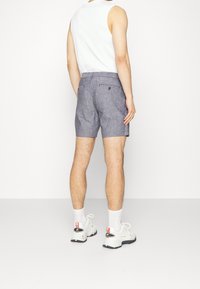 Pánské šedé šortky s texturovanou tkaninou, zadními kapsami a úzkým střihem, v kombinaci s bílým bezrukávem a bílými teniskami.