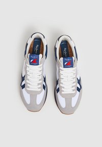Sneakers da uomo con una tomaia in rete bianca, dettagli in suede grigio, elementi di design blu navy e un'etichetta blu con il marchio sulla linguetta.