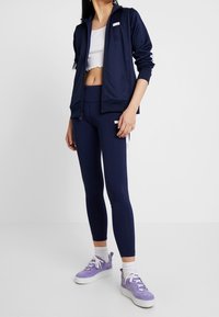 Námořnická mikina na zip s bílými detaily, doplněná o ladící legíny. Modelka má na sobě světle fialové tenisky na platformě a bílé ponožky.