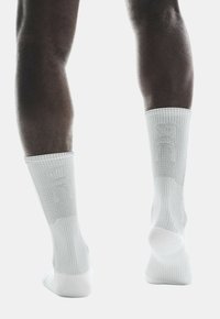 Calzini sportivi bianchi con texture a costine, lunghezza alla caviglia e tallone rinforzato. Presentano un discreto logo del marchio vicino al polpaccio.