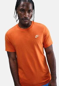 Camiseta de algodón naranja con cuello redondo y un pequeño logo blanco de Nike en el pecho. Manga corta y textura suave.